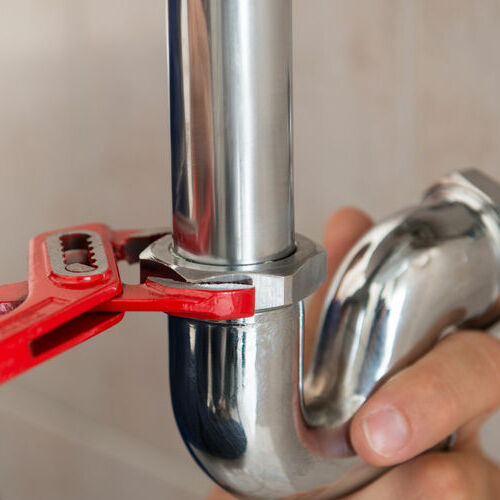A Plumber Tightens a Pipe With a Wrench.