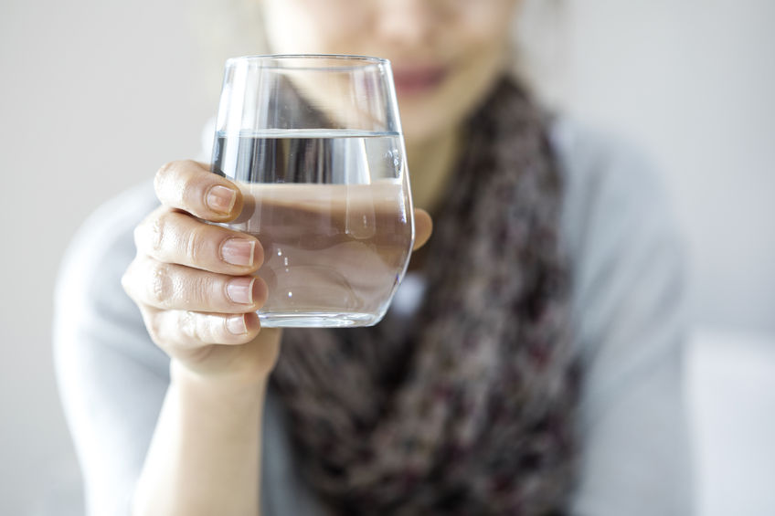 Women faded in background with focus on her hand holding a glass of water.